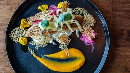 A piece of fish topped with shaved vegetables and crisp style garnishes