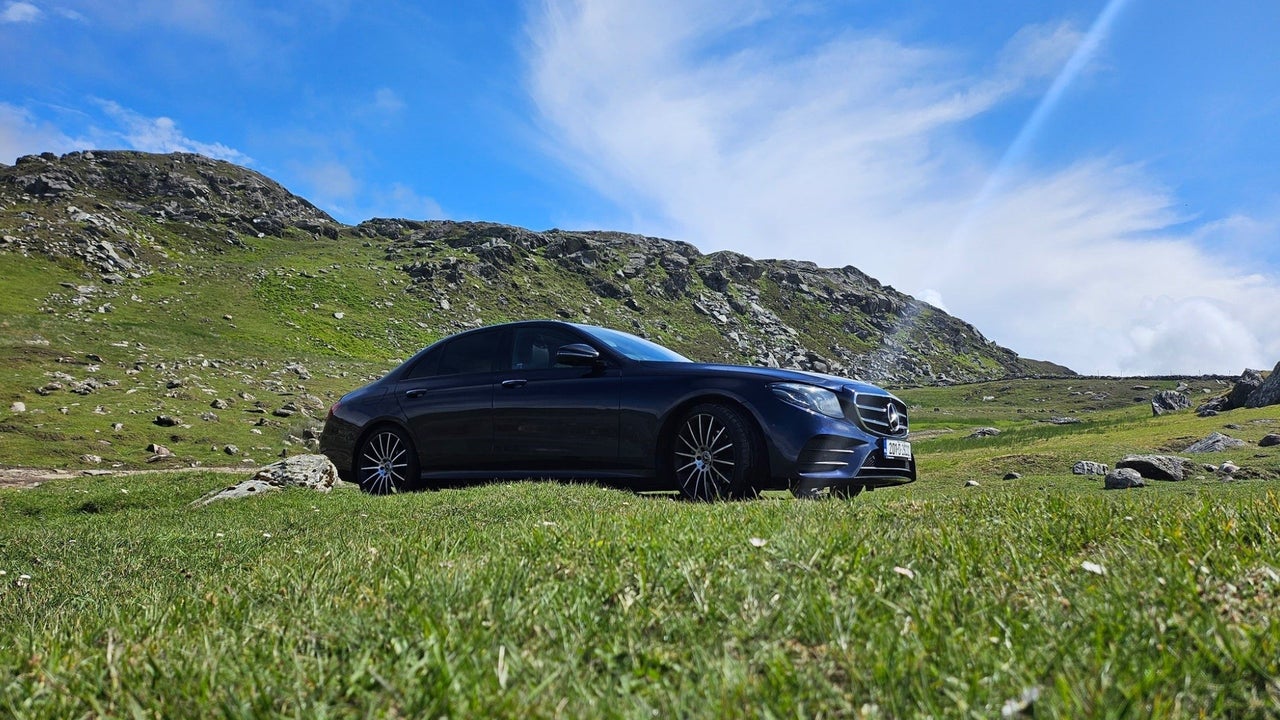 Luxury car parked among greenery with mountains in the background