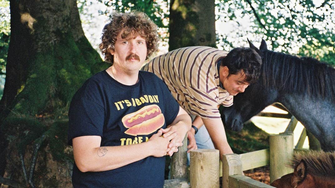 2 people outdoors beside wooden fence holding back horses