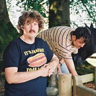 2 people outdoors beside wooden fence holding back horses