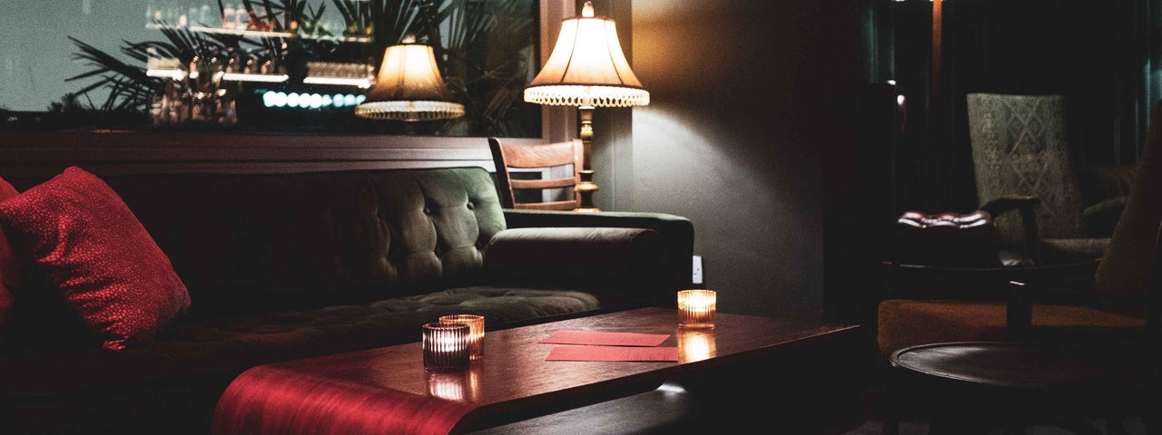 Dark coloured sofa and seating area with muted red coloured accessories and menus on a low table.