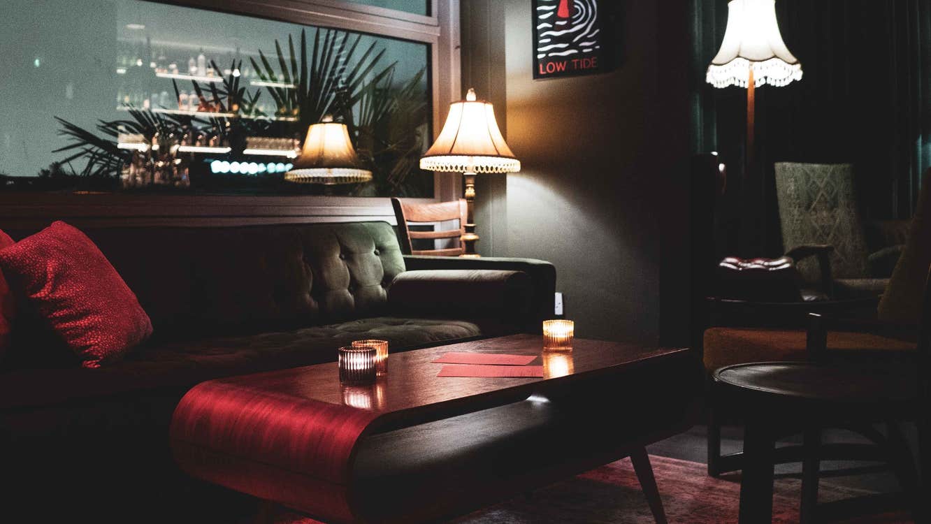 Dark coloured sofa and seating area with muted red coloured accessories and menus on a low table.