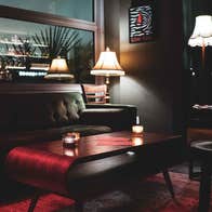 Dark coloured sofa and seating area with muted red coloured accessories and menus on a low table.