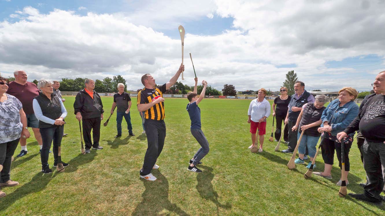 Hurling Tours Ireland view of a group watching a boy and the instructor demonstrating the use of hurleys