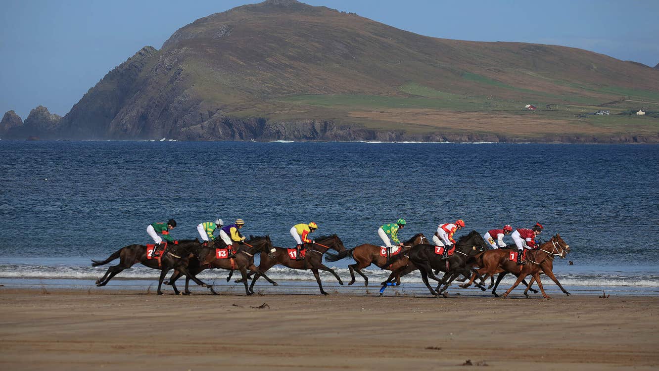 Horse racing on a beach with sea and mountain behind