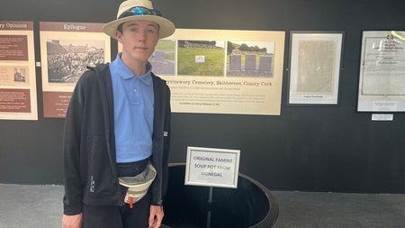 Person standing beside a black soup pot from the famine with storyboards in the background