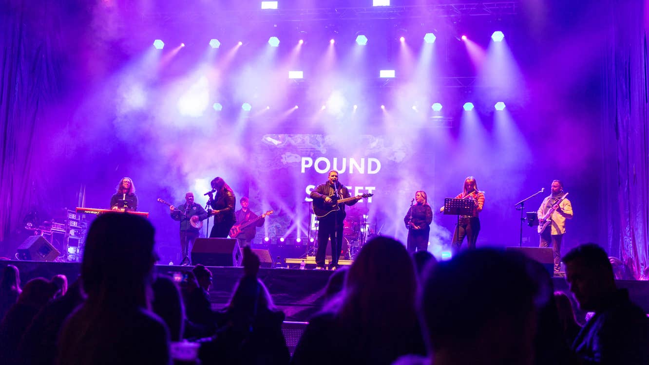 View of a band playing on a stage with purple and white lights.