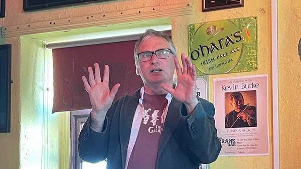 A storyteller in a pub with his hands raised to emphasise a point