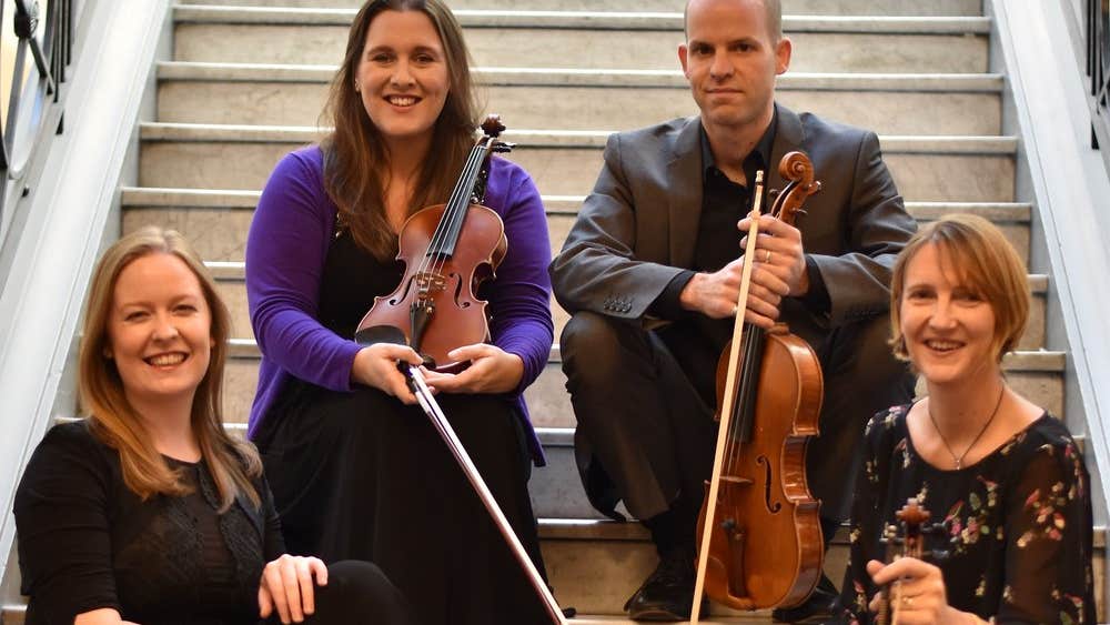The members of the Ficino Quartet are sitting on a staircase with their instruments.