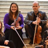The members of the Ficino Quartet are sitting on a staircase with their instruments.