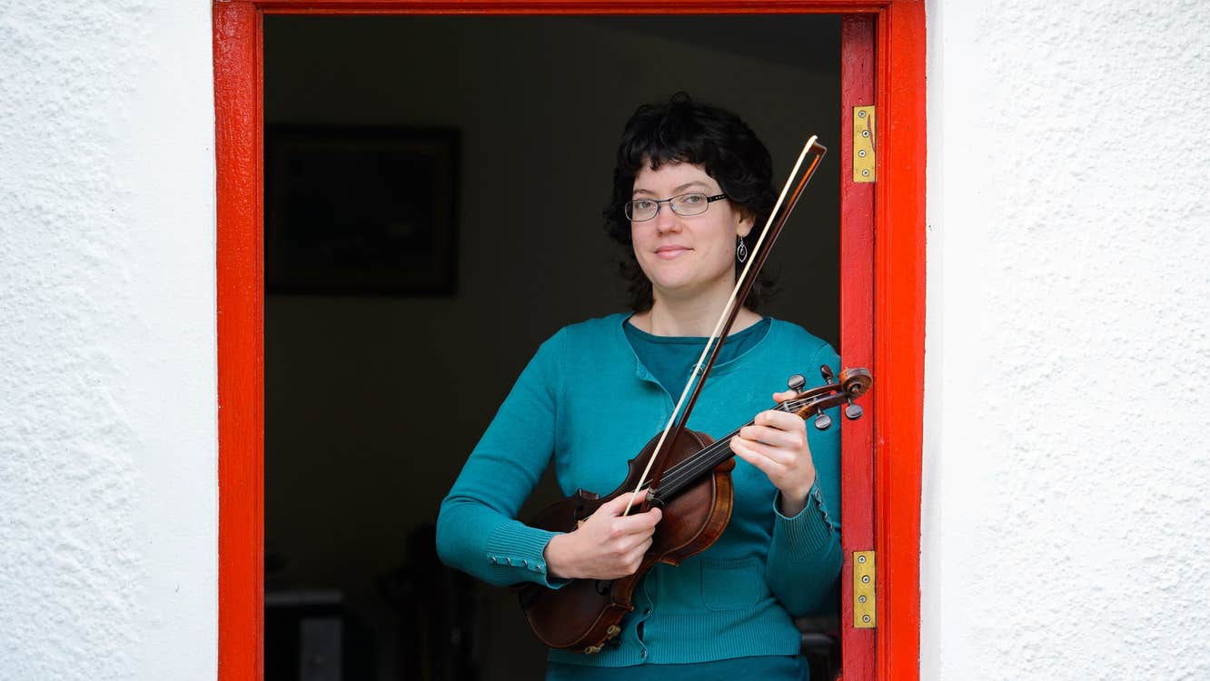 Person holding a fiddle in a red half doorway with the bottom half closed