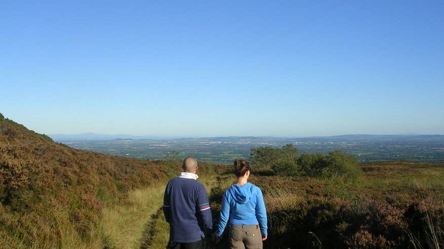 A man and woman holding hands looking out at blue skies and mountain views