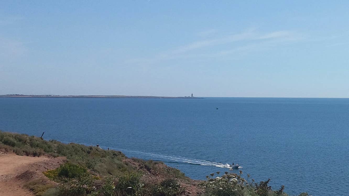 Boat in sea beneath Dunmore East cliffs with Hook Lighthouse in the distance