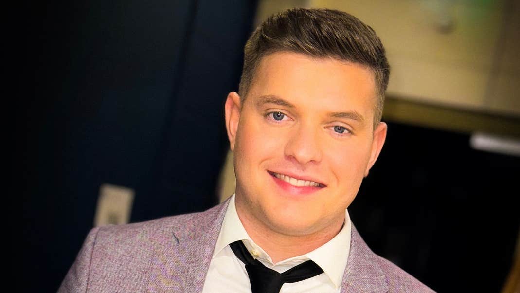 A smiling man in black tie and light grey jacket.