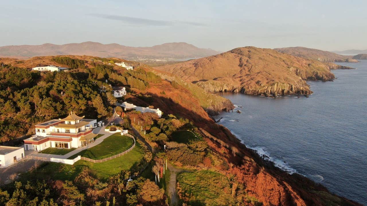 An aerial view of a building resembling a small Tibetan monastery perched on a cliff