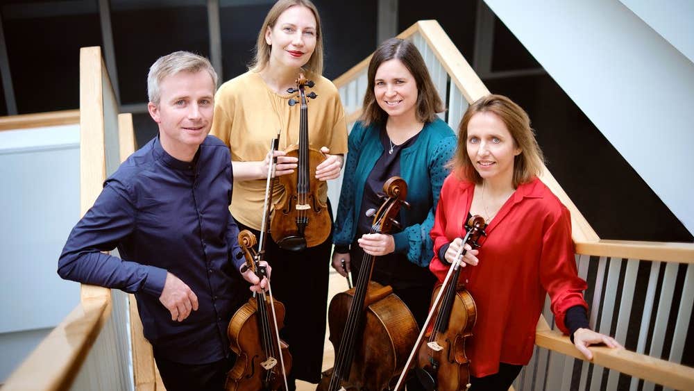 The members of the Solas Quartet are standing on a staircase, holding their instruments.
