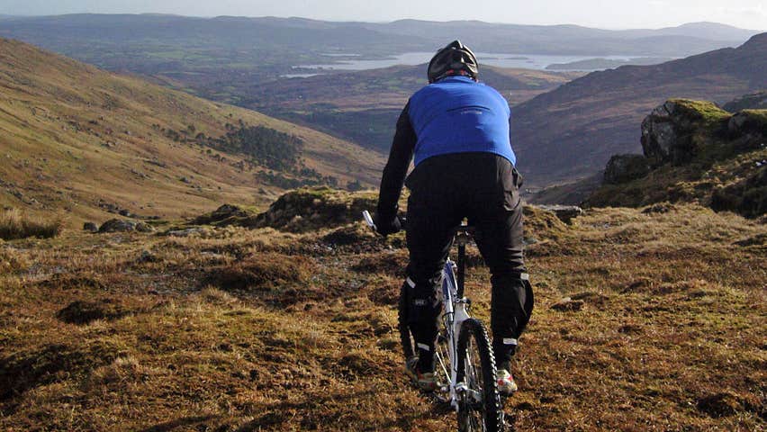A man sitting on a mountain bike wearing a blue cycyling top looking out over a mountainscape expanse