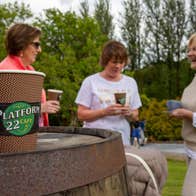 Three ladies outside having coffee with a take away coffee cup on a barrel to the forefront