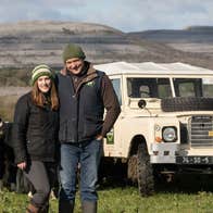 Couple in field with cows and jeep with mountain view