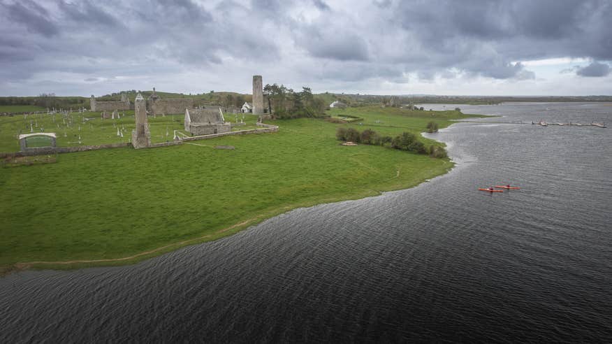 Two people kayaking past ruins on the coastline