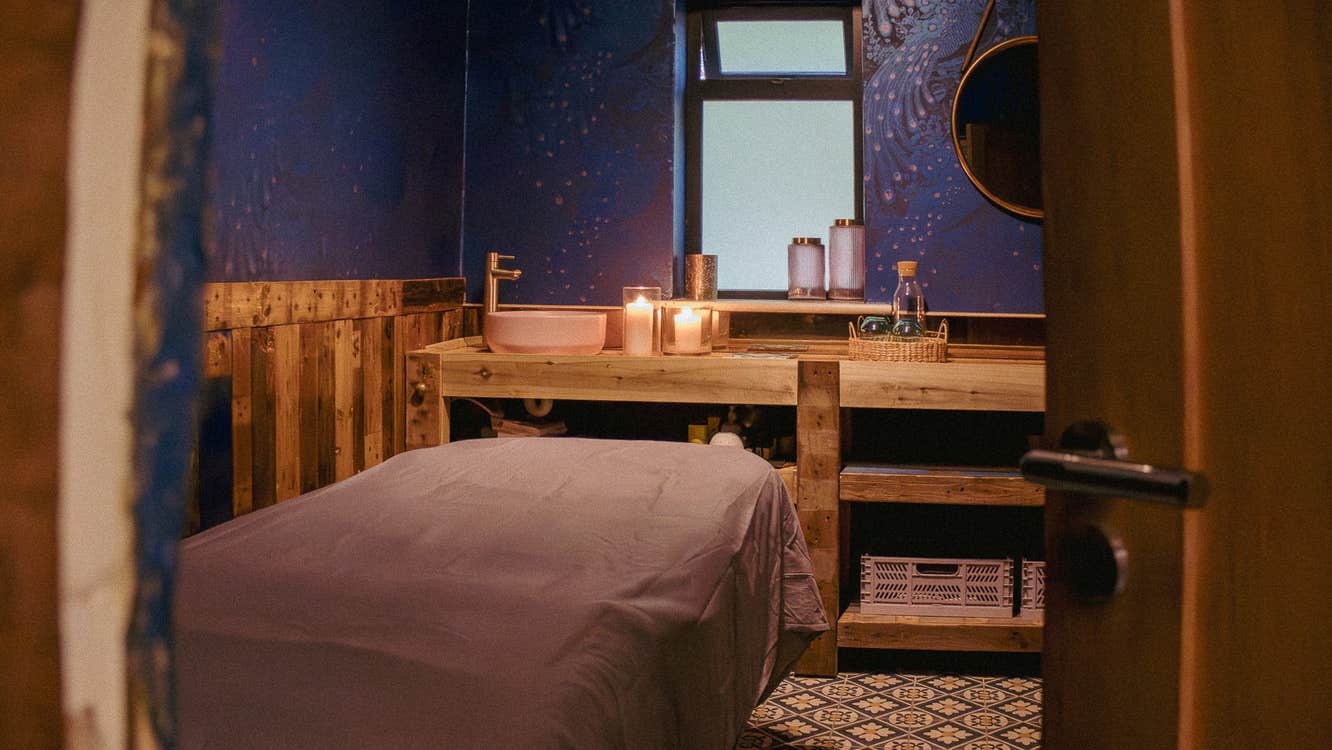 Spa treatment room with a table and pink basin and candles on wooden shelving