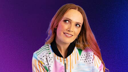 A woman smiling, looking upwards to her right, against plain blue to purple background.