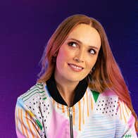 A woman smiling, looking upwards to her right, against plain blue to purple background.