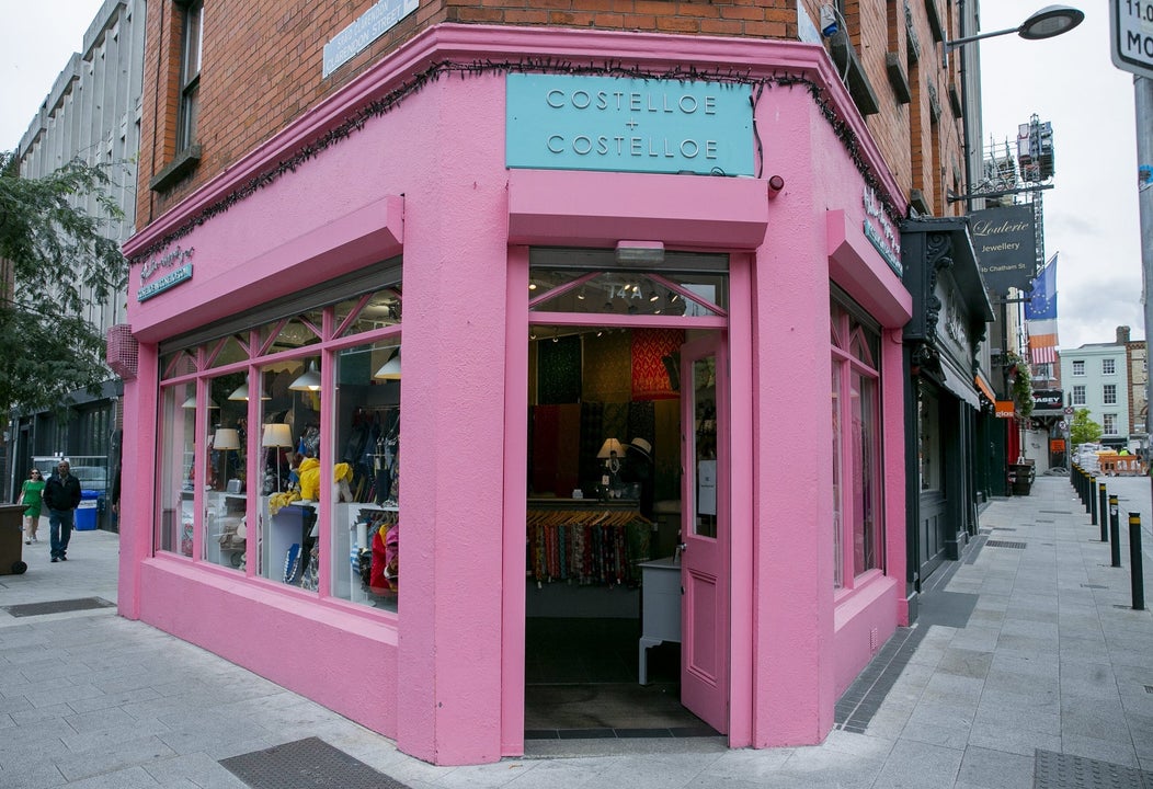 Street view of a pink shop on a corner with a blue sign above an open door