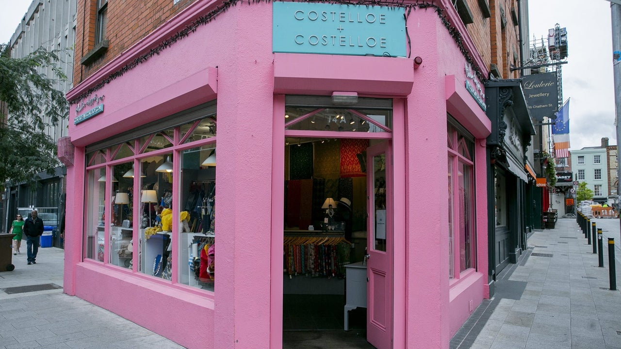 Street view of a pink shop on a corner with a blue sign above an open door