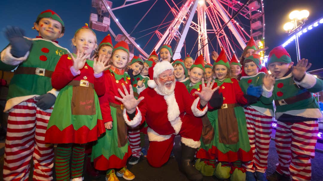 Waterford Winterval Festival 2026, a santa kneeling with jazz hands surrounded by children dressed as elves.