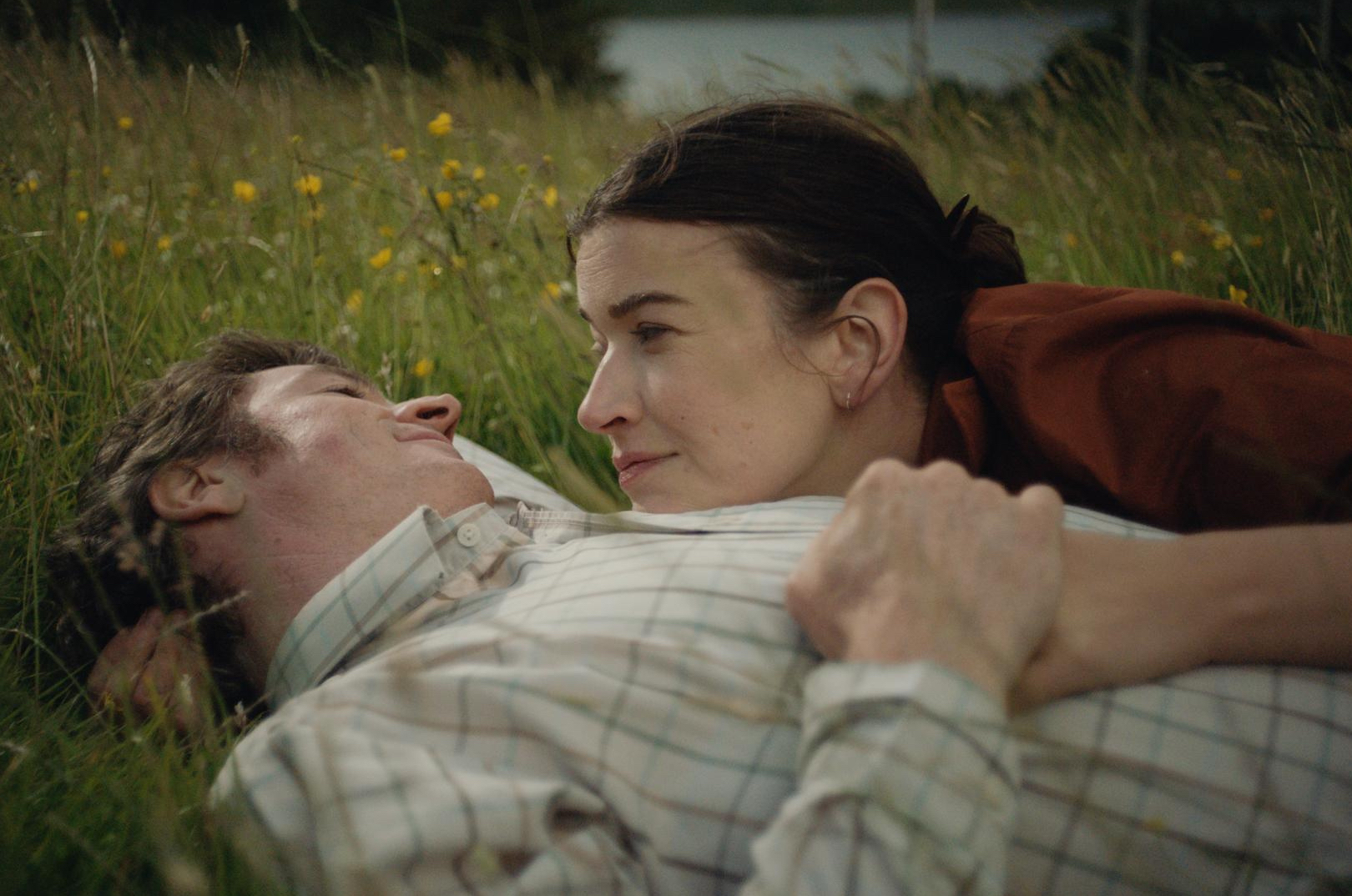 A man and woman are laying together in a field.