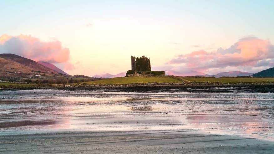A castle beside a river against a backdrop of pastel pink skies in Cahersiveen, Kerry