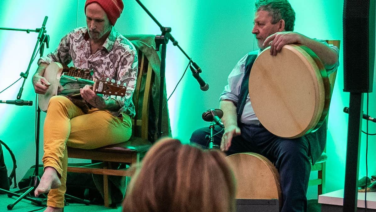 2 seated men with musical instruments on a small stage.