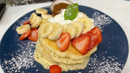 A plate of American style pancakes with whipped cream bananas and strawberries at Sweet Churro