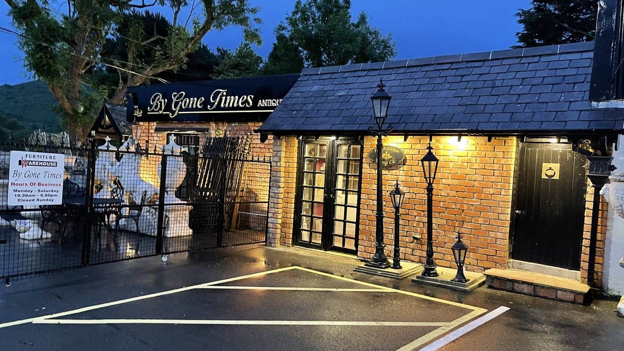 An antique shop exterior lit up at dusk with antique lamp posts outside