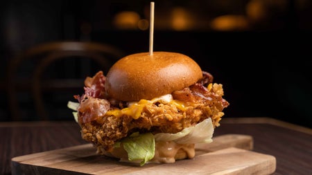 Burger with a large cocktail stick through it on a wooden serving tray