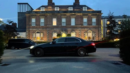 Long black car outside a large stone building at dusk