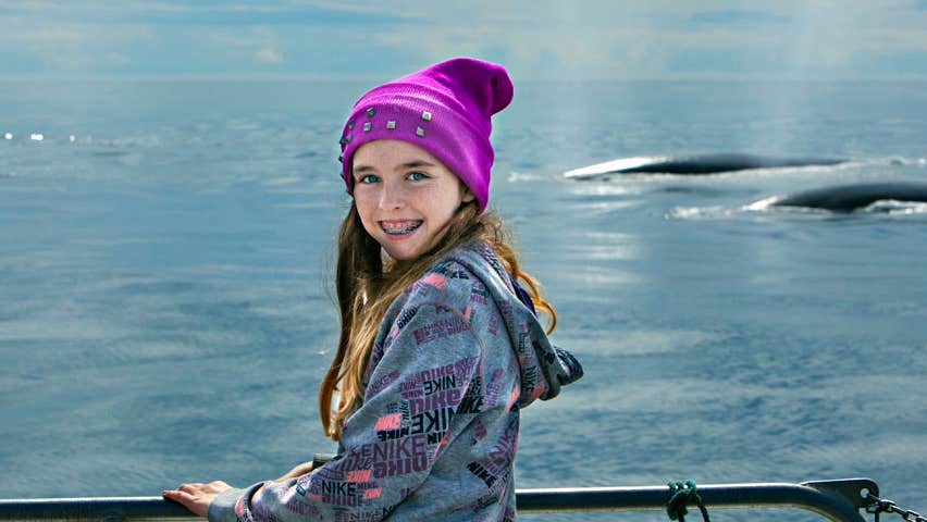 Image of girl on a boat with two dolphins in the background