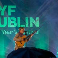 NYF Dublin, Traditional Music Concert - a man playing a guitar and singing on a stage, lit behind in green
