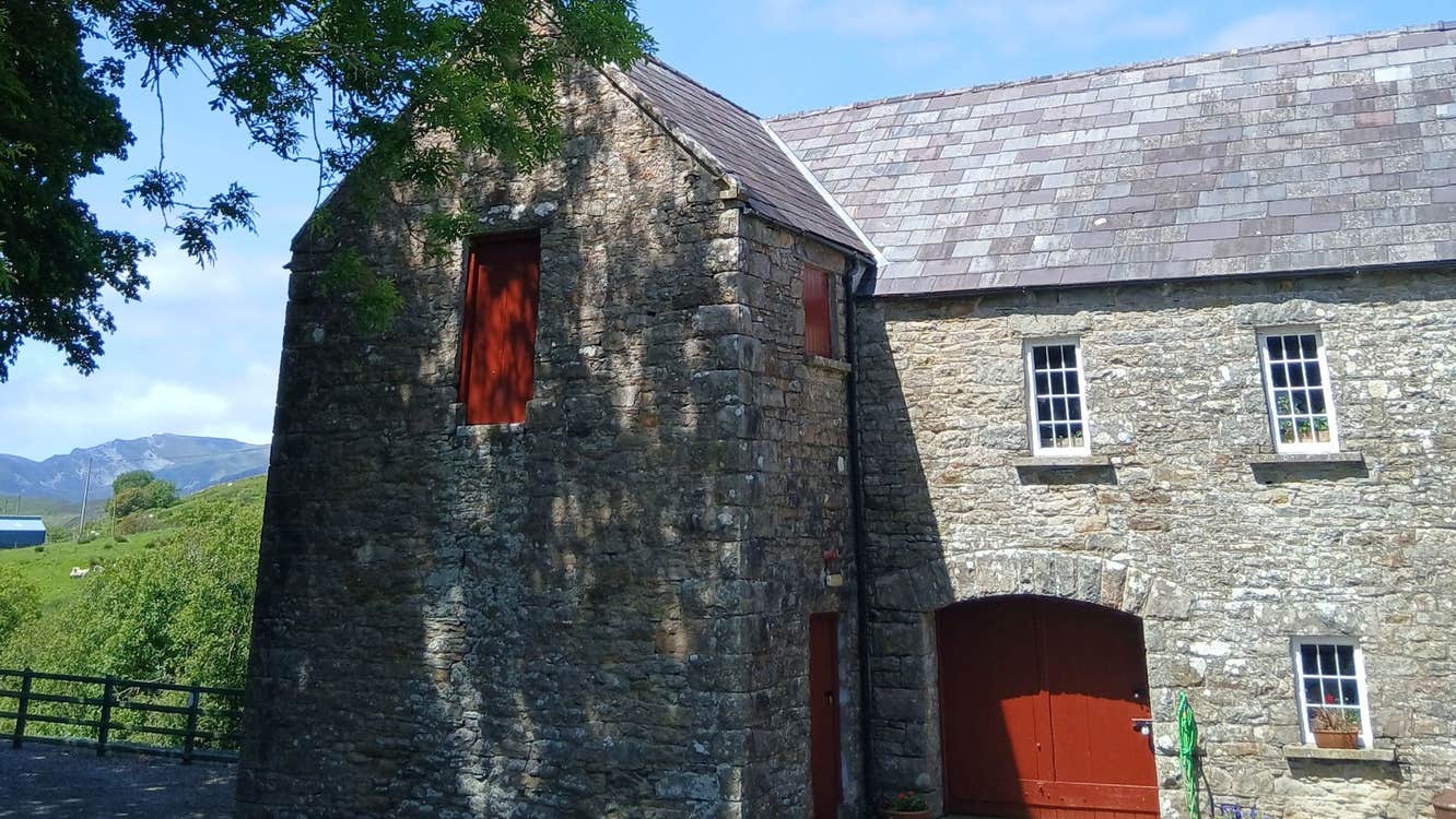 Exterior of a traditional stone corn mill with red doors with trees and hills in the background