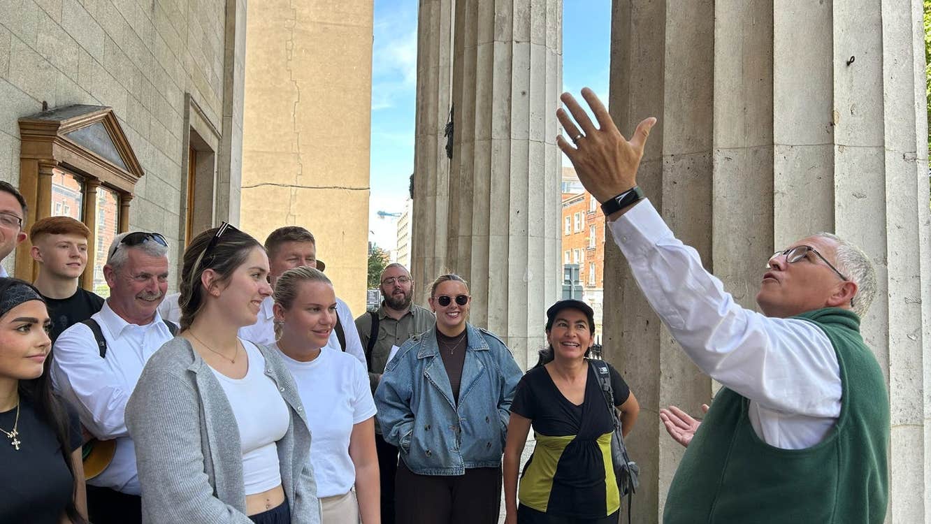 A tour guide and group outside an historic building with tall stone pillars
