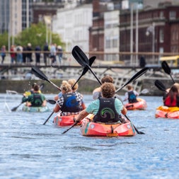 A group of paddlers in kayaks on the River Liffey in Dublin going towards the Ha'penny bridge