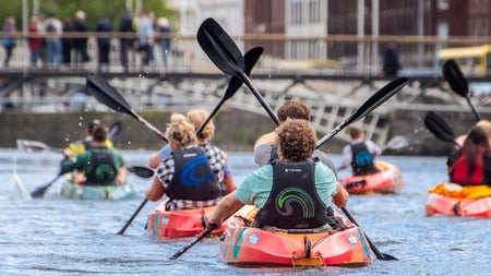 A group of paddlers in kayaks on the River Liffey in Dublin going towards the Ha'penny bridge