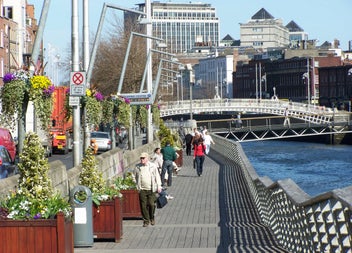 A boardwalk lined with flowers and plants along a river in a city
