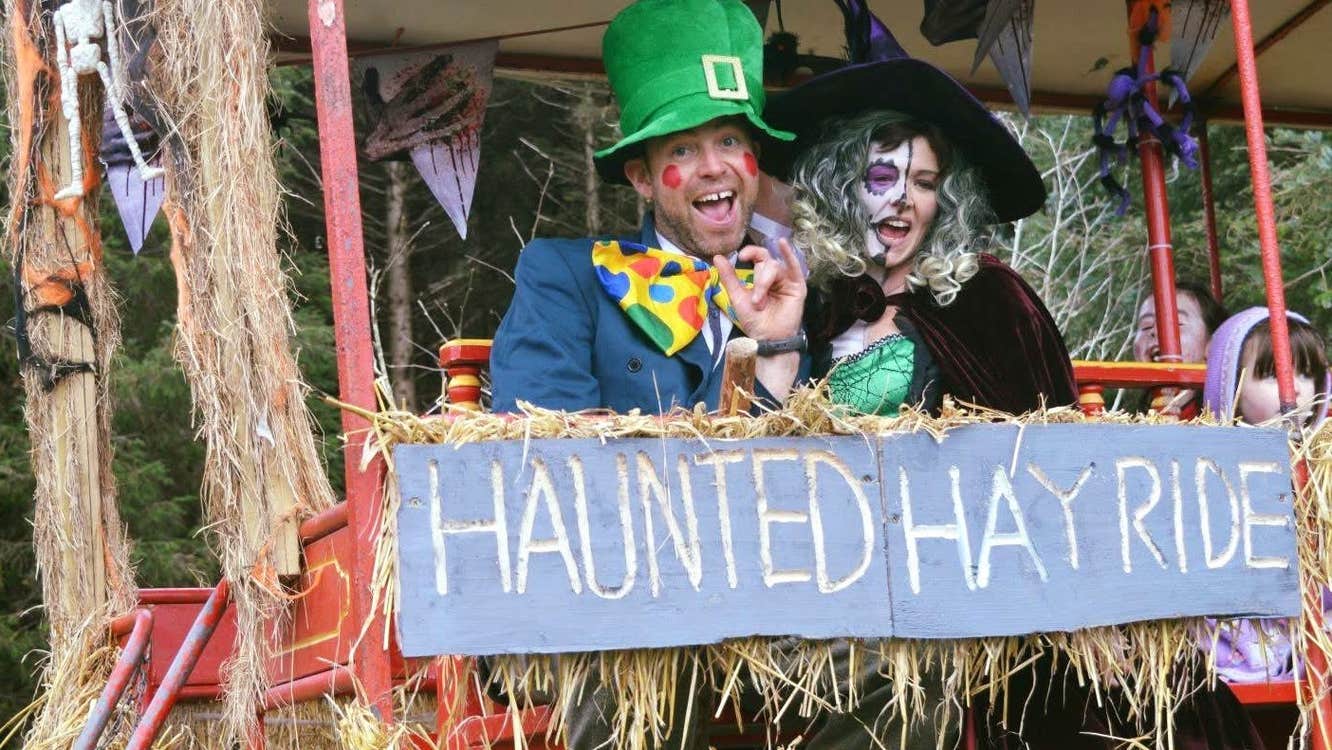A person dressed as a witch beside a person dressed as a leprechaun on a trailer decorated with straw and halloween themed items.