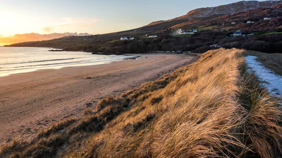Sand dunes and a backdrop of mountains dotted with houses at Fintra Beach, Donegal