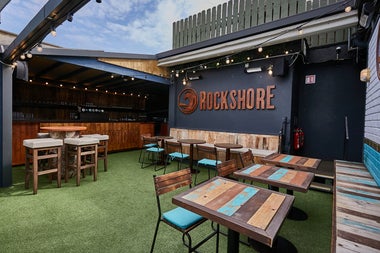 A roofless bar with wooden tables and seating under a blue sky