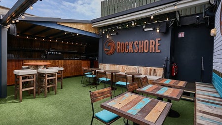 A roofless bar with wooden tables and seating under a blue sky