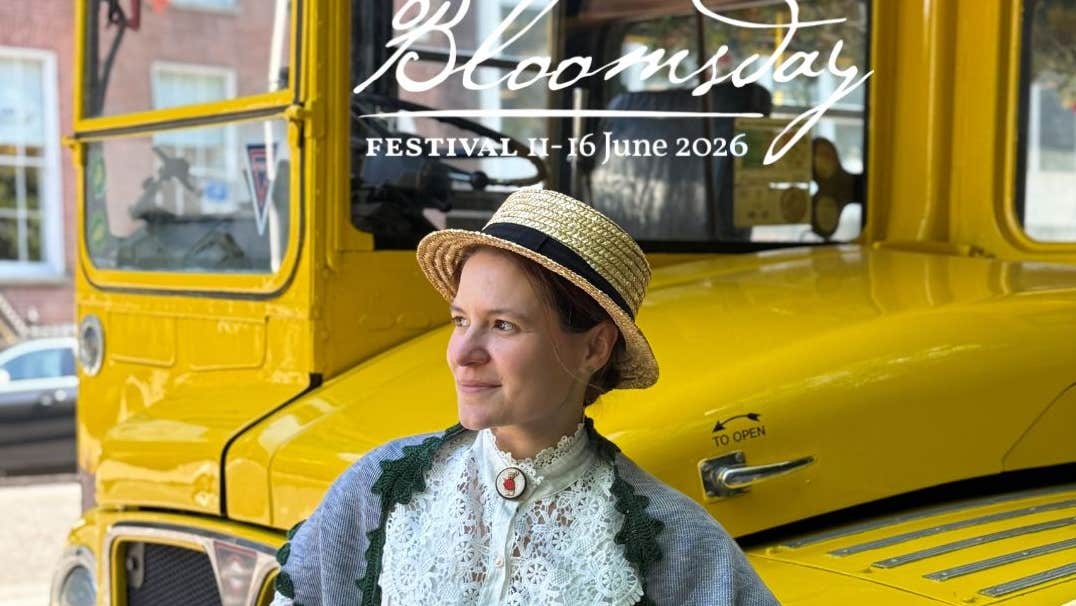 Bloomsday Afternoon Tea Trip, a smiling woman in Edwardian outfit with straw hat standing in front of a vintage yellow bus.
