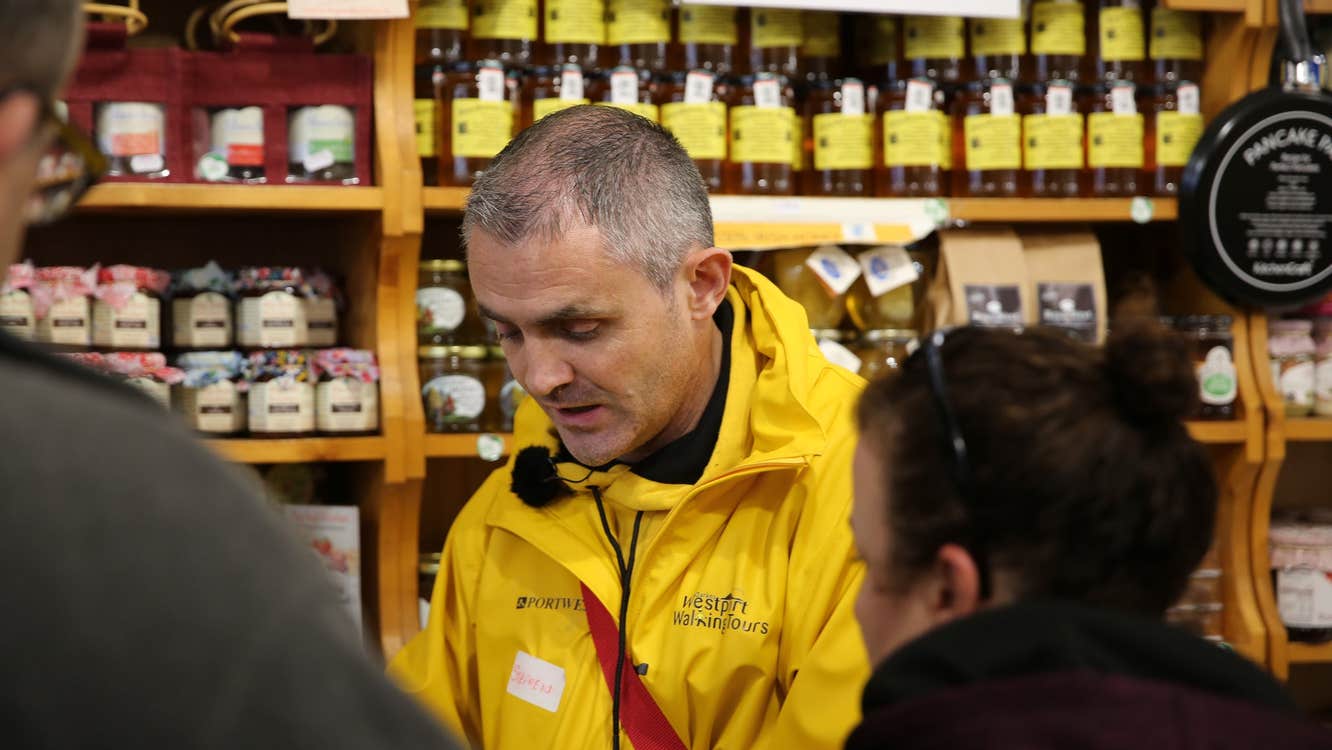 A tour guide discusses a food item with two people standing in foreground